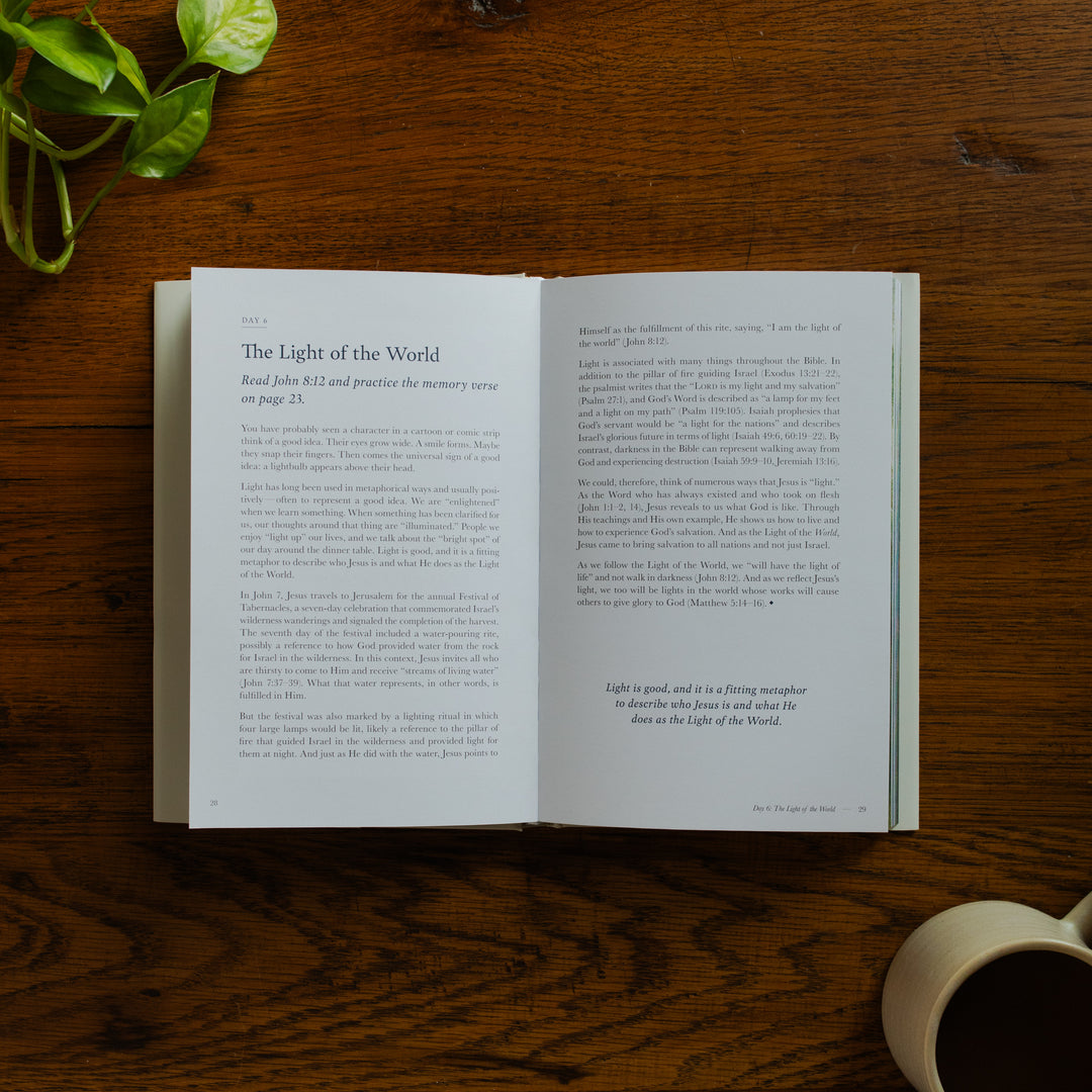 Forty Sayings of Jesus hardcover opened to the Light of the World page near a coffee cup on a wooden table