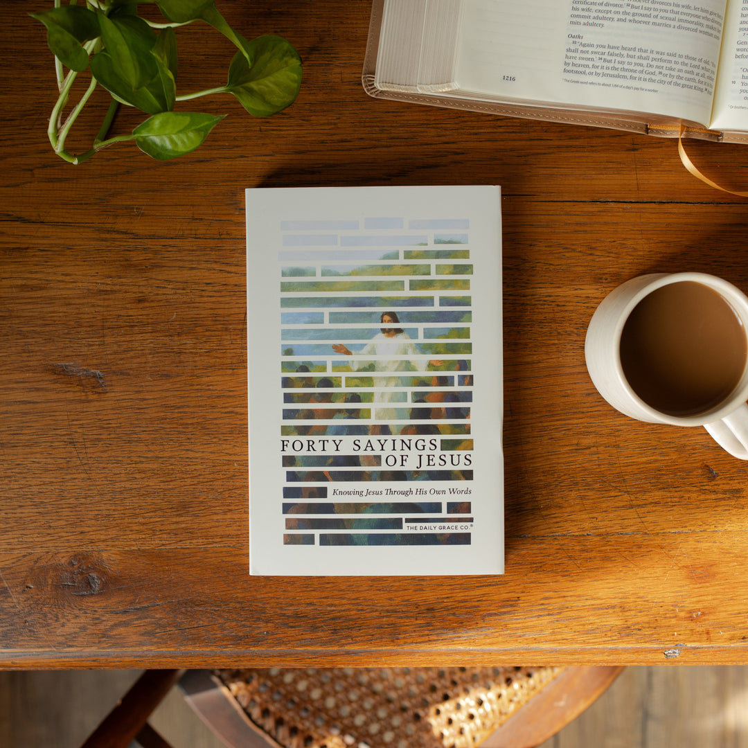 The Forty Sayings of Jesus book on a wooden table next to a white coffee cup and an open bible