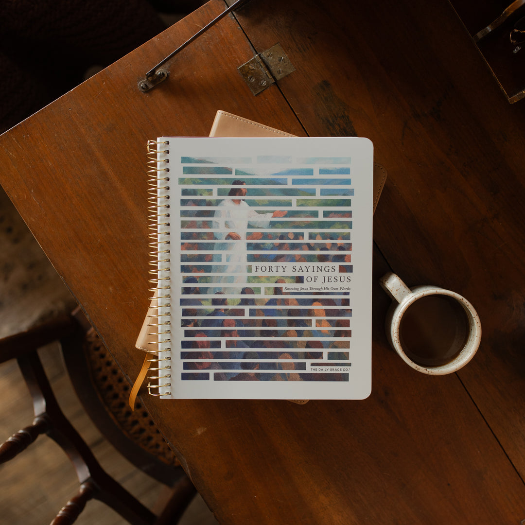 Forty Sayings of Jesus spiral cover on a closed bible near a coffee cup on a wooden table