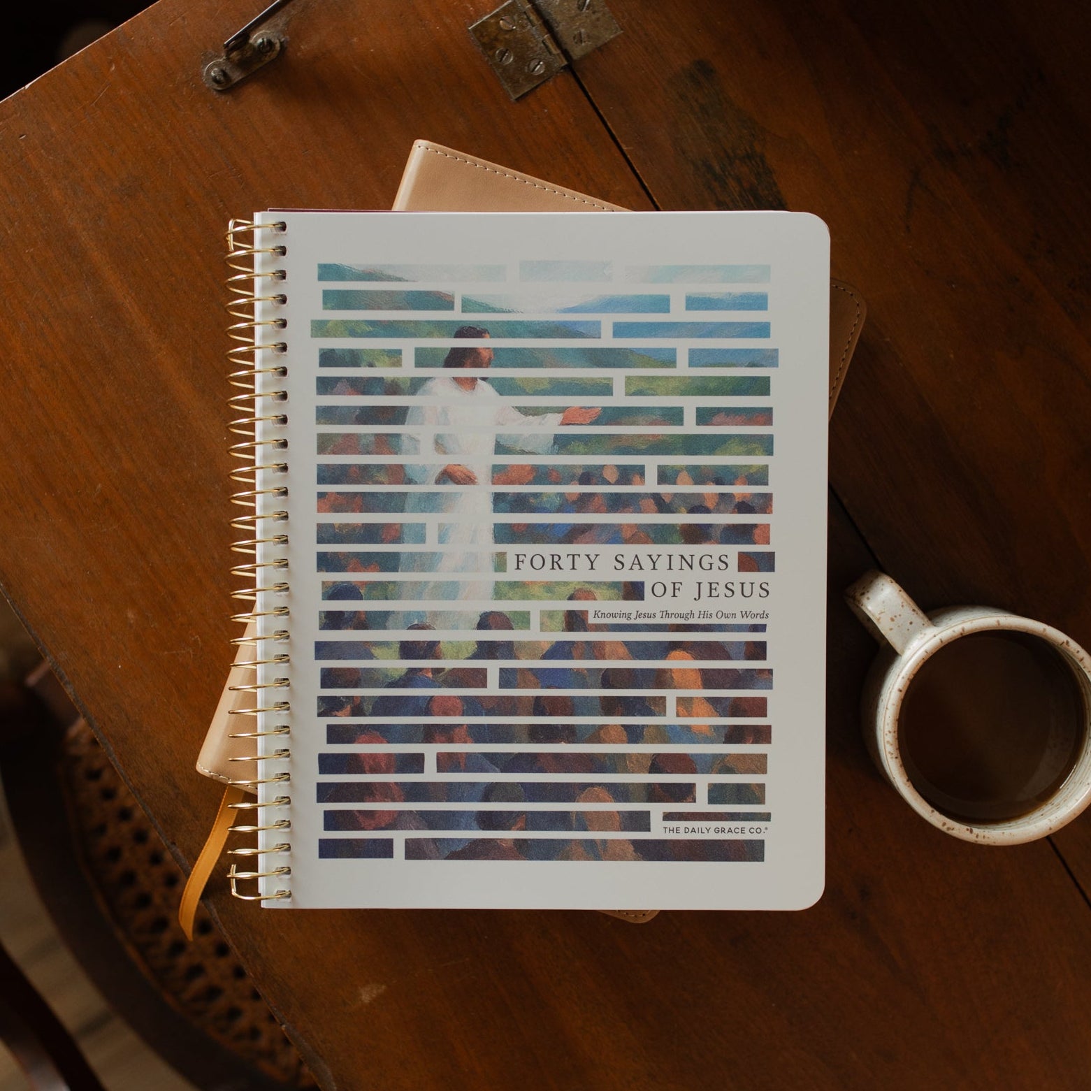 Forty Sayings of Jesus spiral cover on a closed bible near a coffee cup on a wooden table