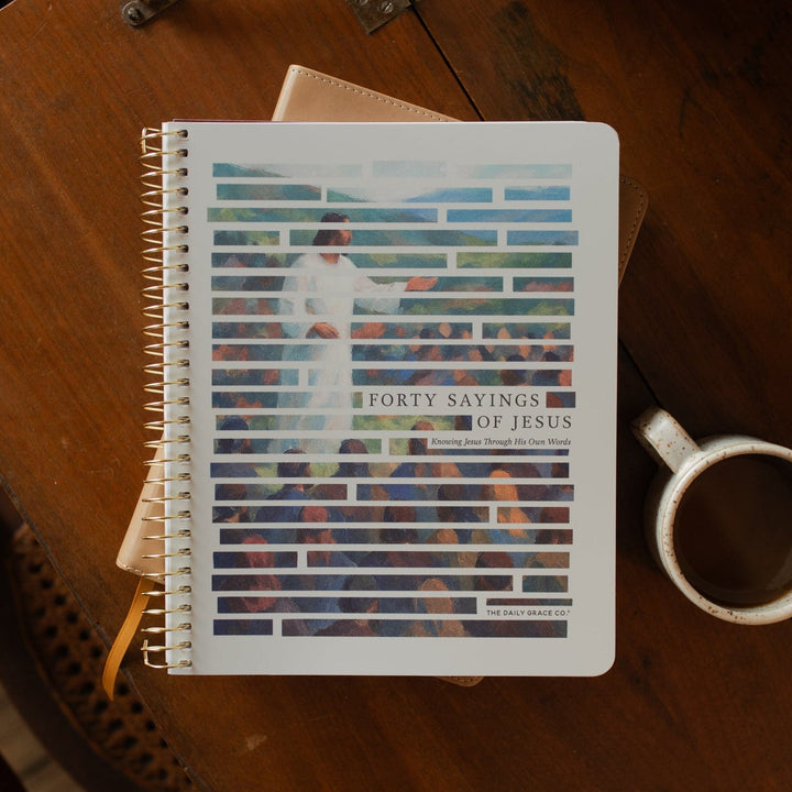 Forty Sayings of Jesus spiral cover on a closed bible near a coffee cup on a wooden table