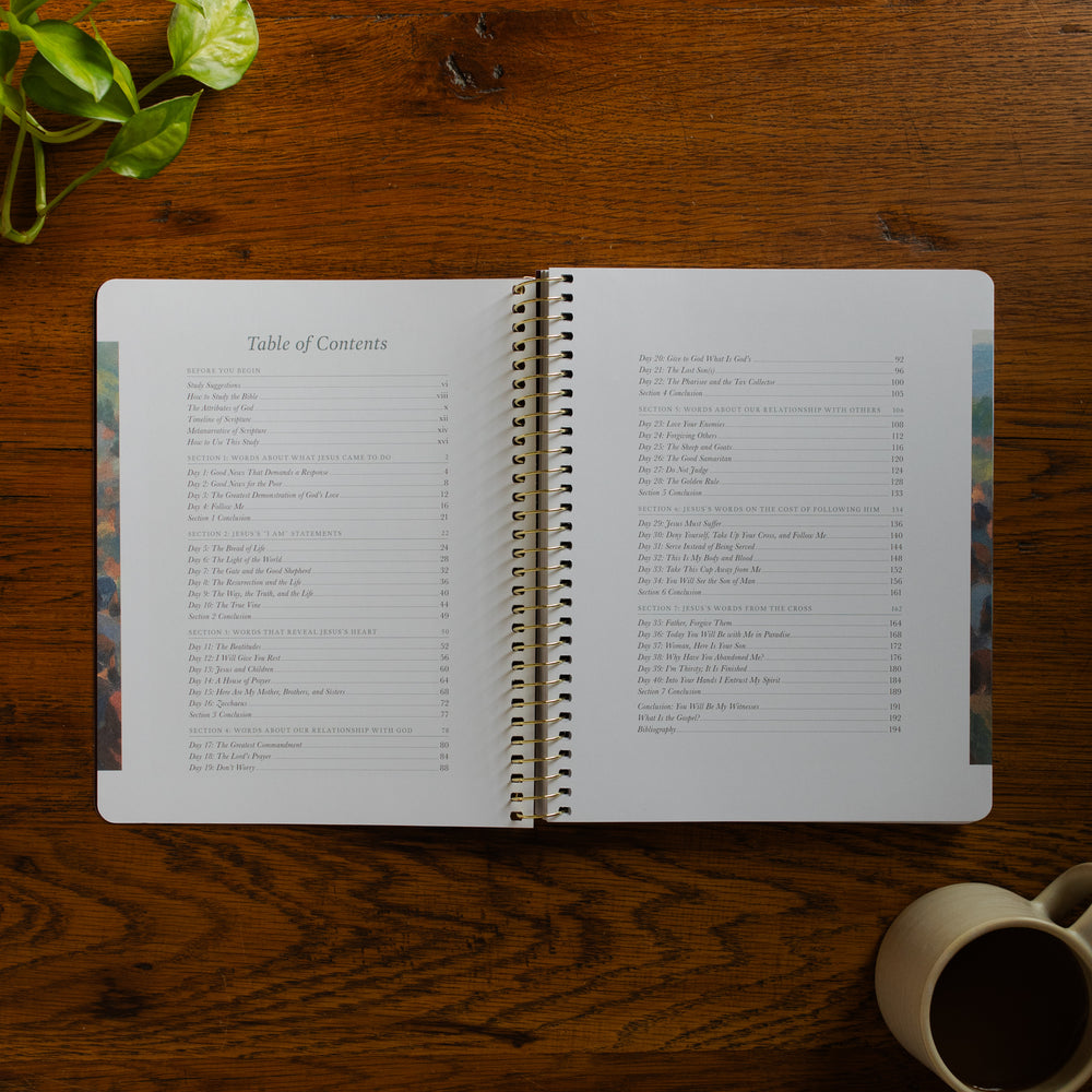 Forty Sayings of Jesus spiral opened to the table of contents near a coffee cup on a wooden table