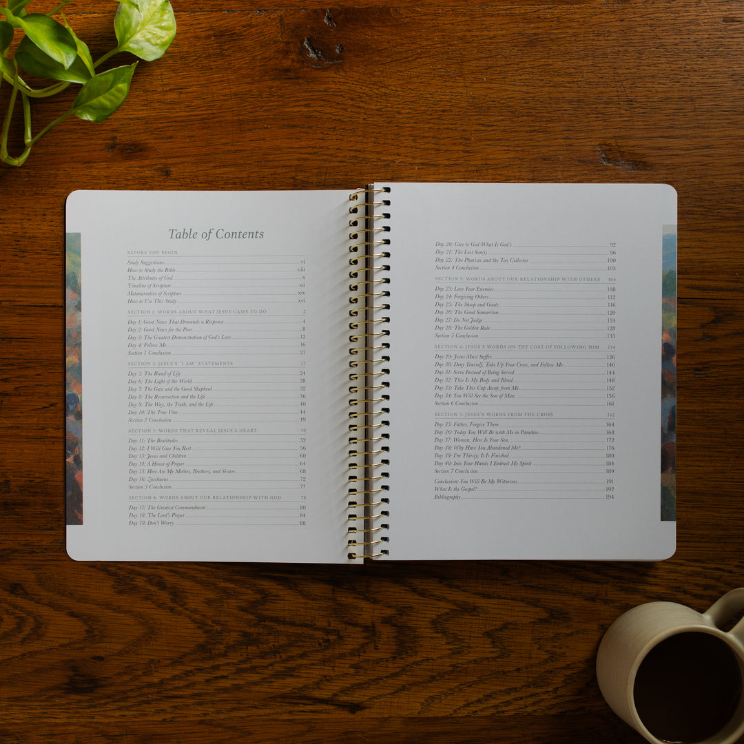 Forty Sayings of Jesus spiral opened to the table of contents near a coffee cup on a wooden table