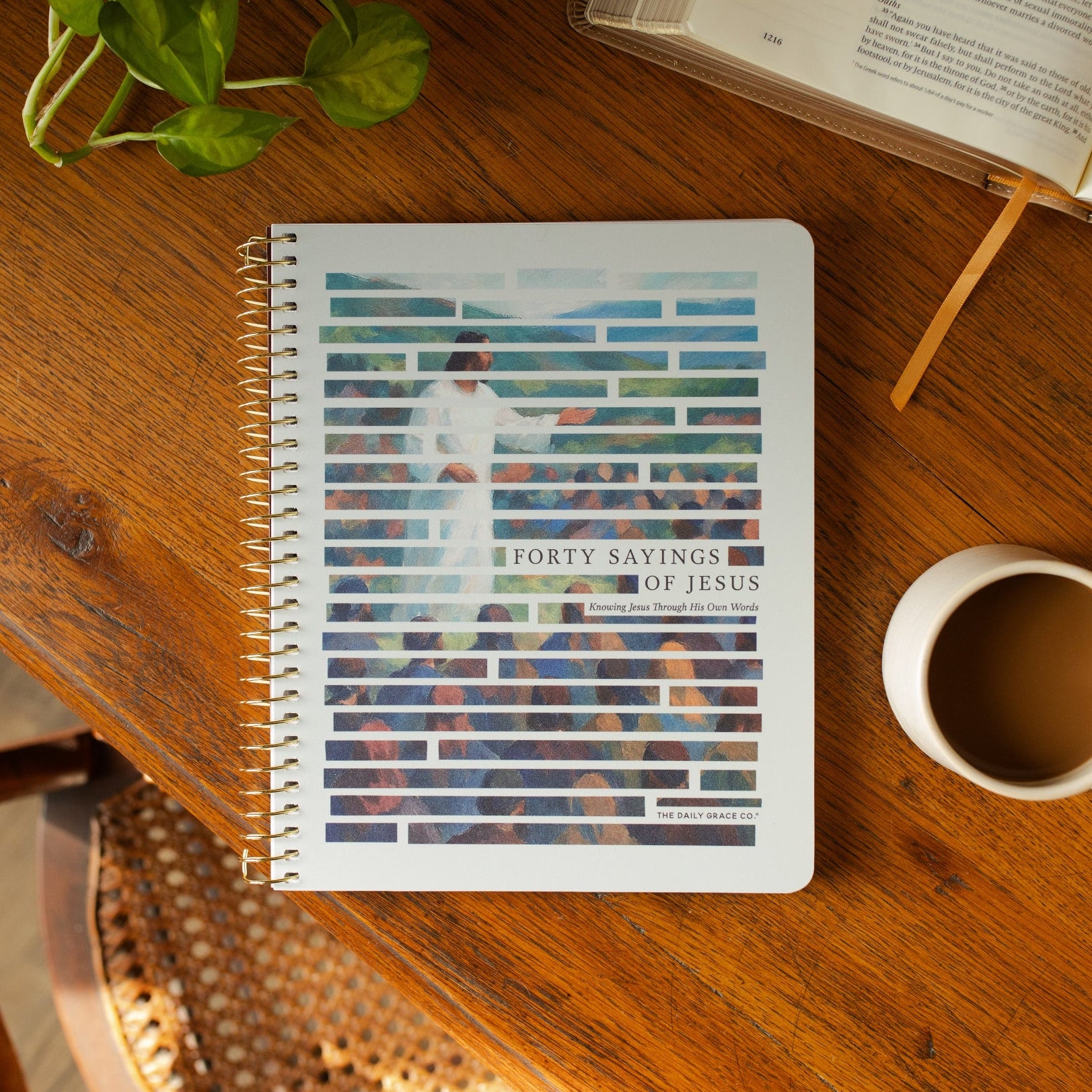 The Forty Sayings of Jesus Spiral cover on a wooden table next to a white coffee cup and an open bible