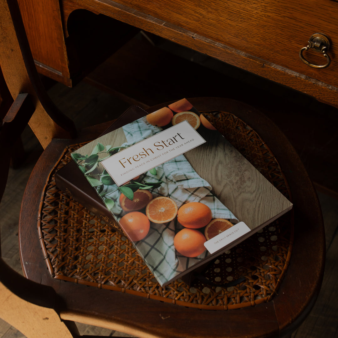 Fresh Start Bible study cover on a wooden woven chair stacked on top of another book next to a wooden table