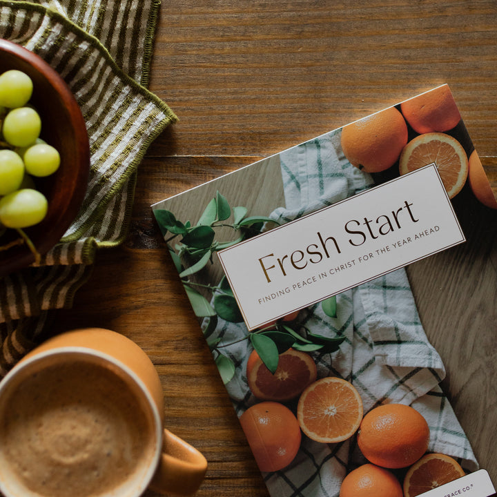 Fresh Start Bible cover on a wooden table next a green striped towel and a bowl of grapes and a cup of coffee