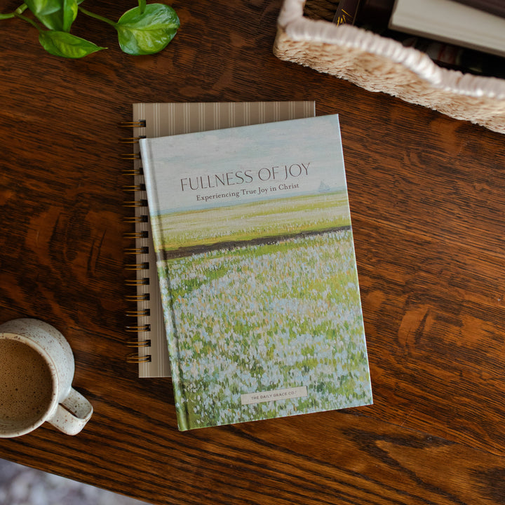 The Fullness of Joy cover on a closed journal on a wooden table next to a coffee cup