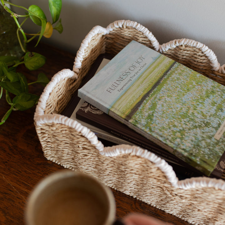 The Fullness of Joy cover on a stack of other daily grace books in a woven basket next to a coffee cup