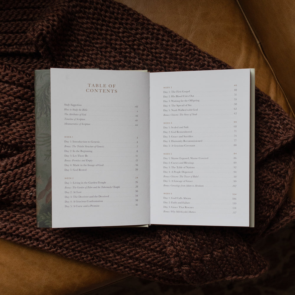 Genesis Hardcover study opened to the table of contents page on a woven blanket on a leather couch