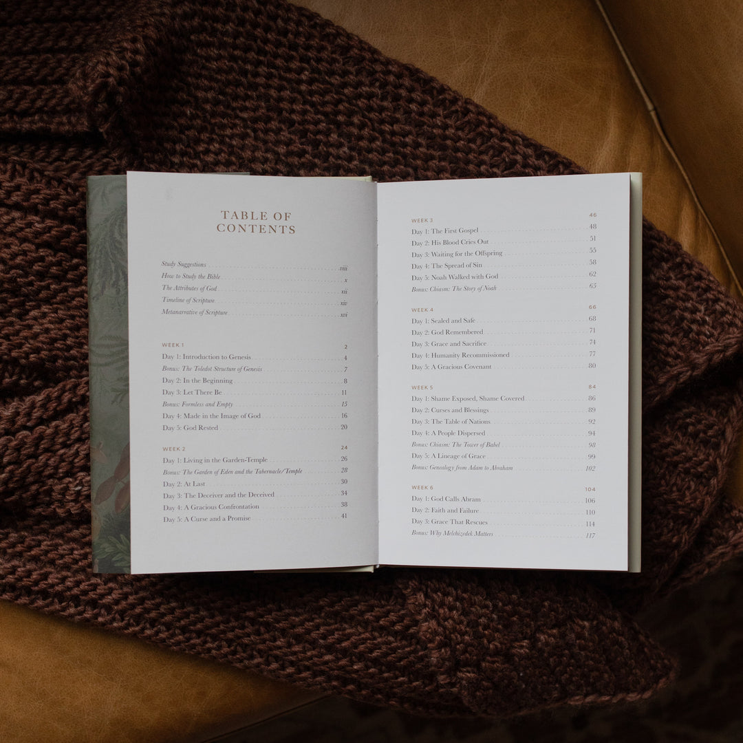 Genesis Hardcover study opened to the table of contents page on a woven blanket on a leather couch