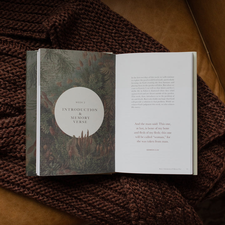 Genesis Hardcover study opened to the week 2 introduction page on a woven blanket on a leather couch