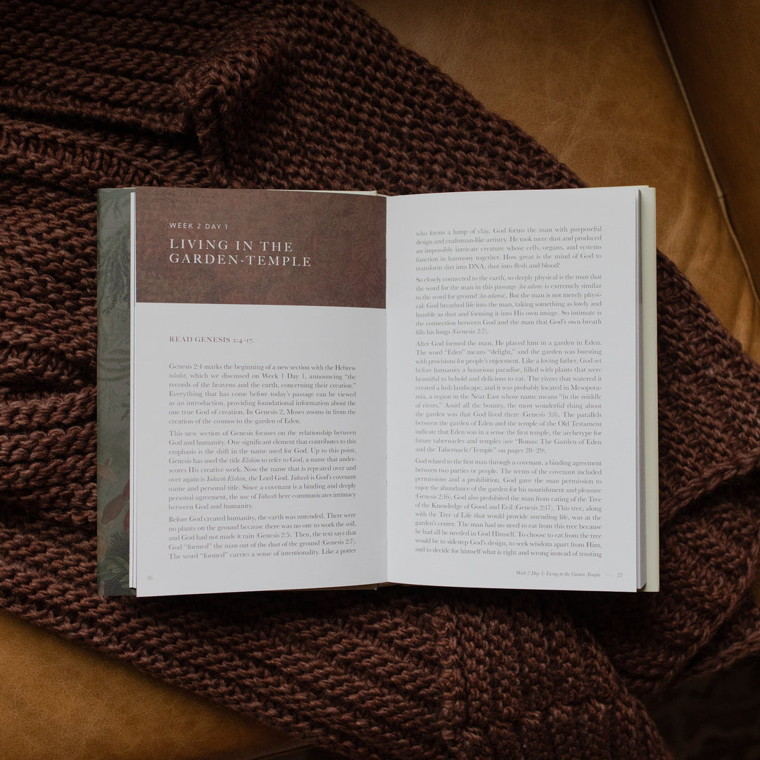 Genesis Hardcover study opened to the Week 2 Day 1 Reading page on a woven blanket on a leather couch