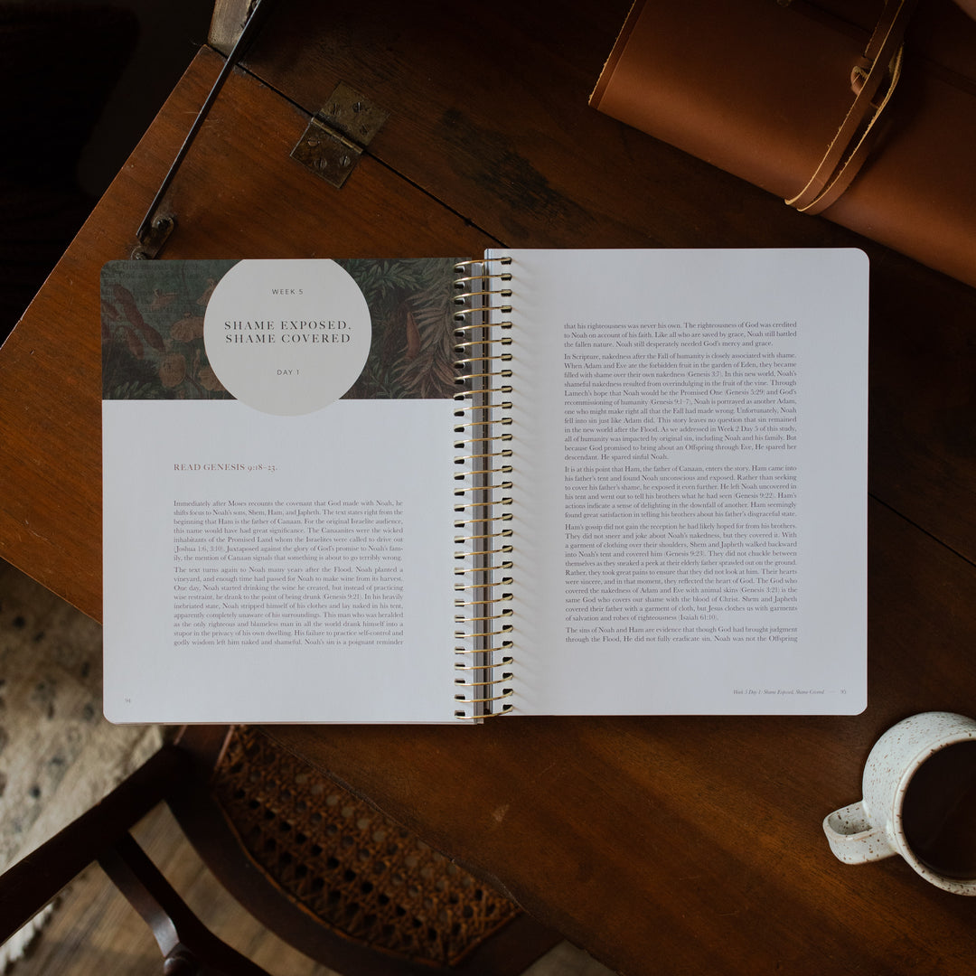 Genesis Spiral opened to the week 5 reading page on a wooden table near a coffee cup