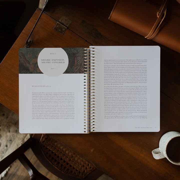 Genesis Spiral opened to the week 5 reading page on a wooden table near a coffee cup