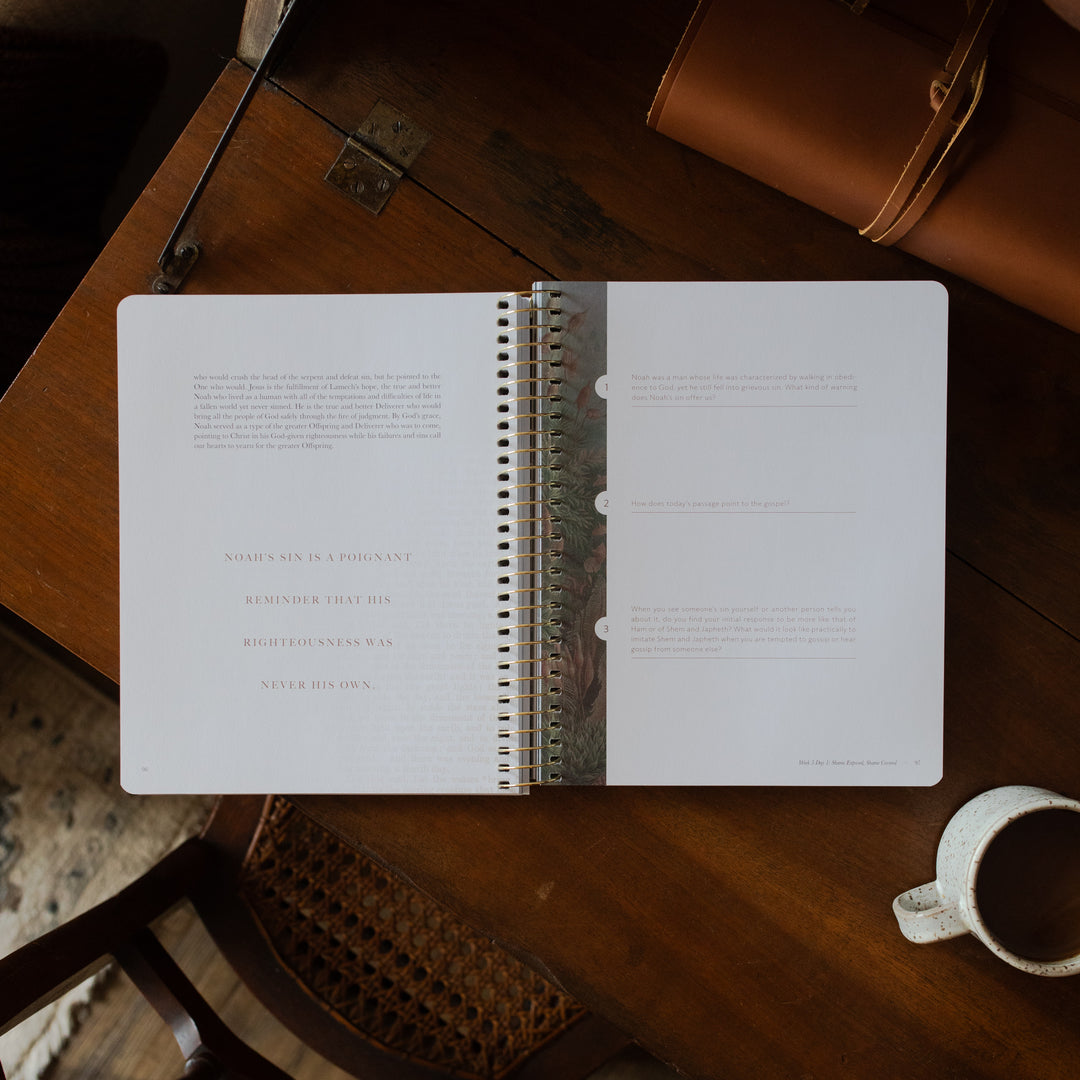 Genesis Spiral opened to the applications and questions page on a wooden table near a coffee cup