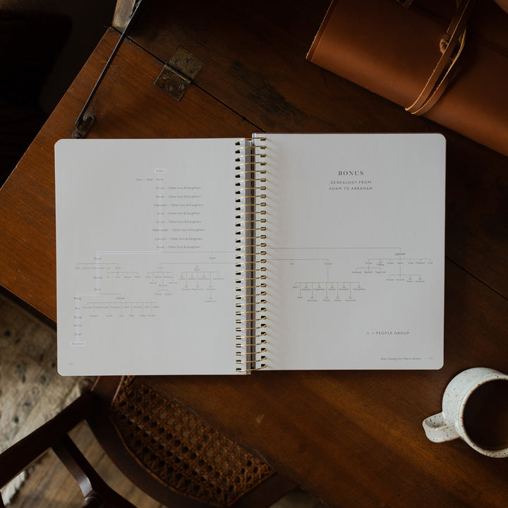 Genesis Spiral opened to the bonus page on a wooden table near a coffee cup