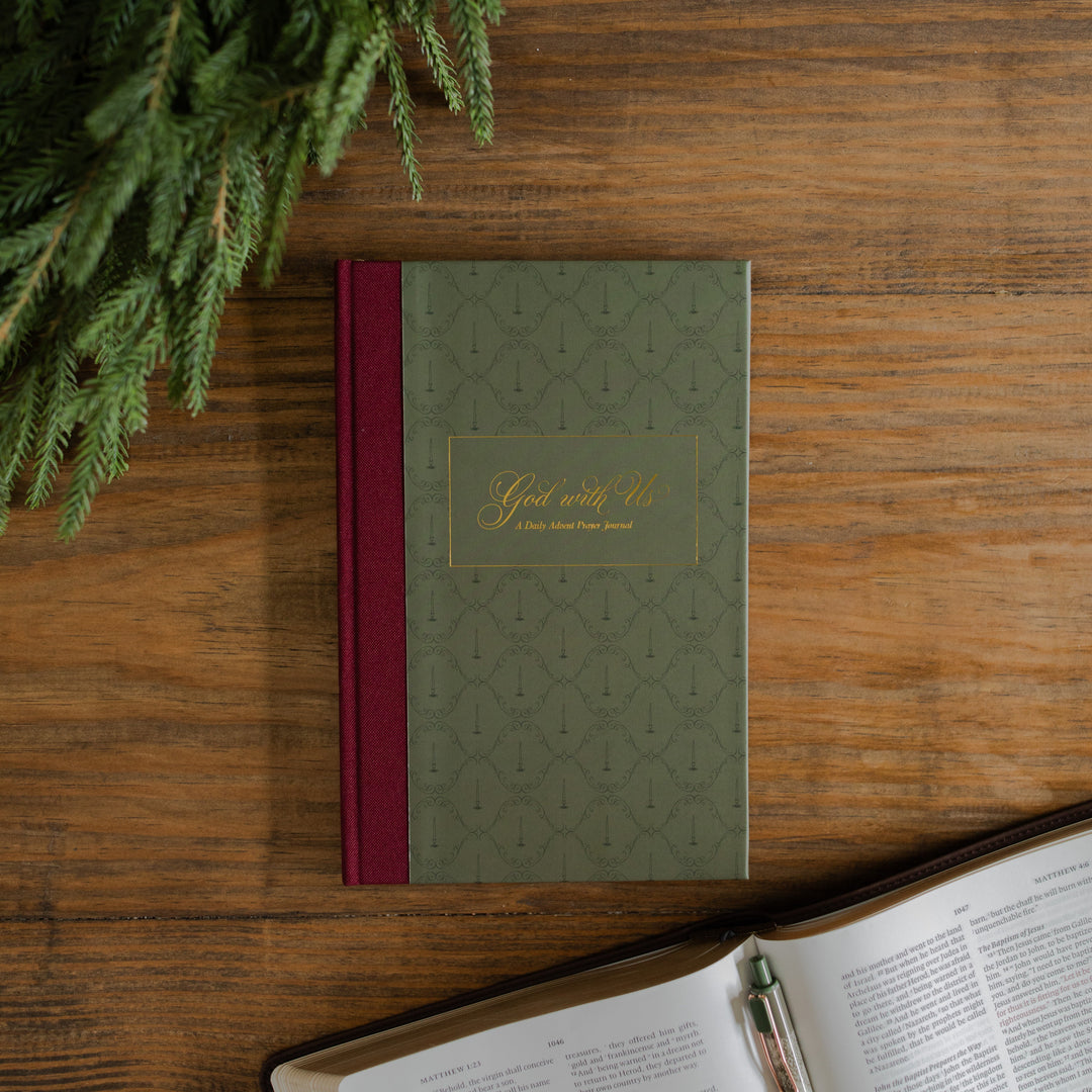 God with Us Prayer Journal cover on a wooden desk next to some greenery and an open bible