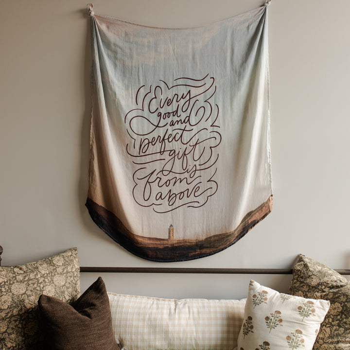 Good and Perfect Gift Swaddle hanging on a wall over a couch with pillows