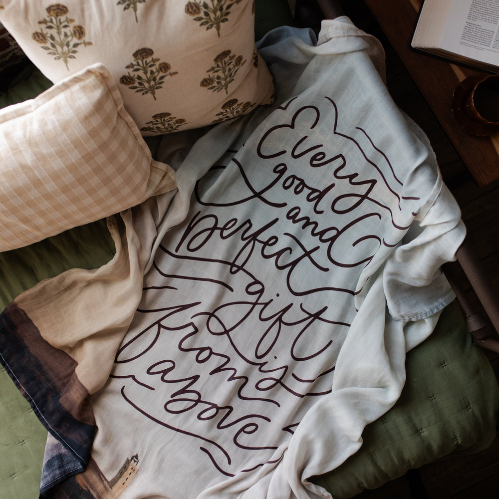 Good and Perfect Gift Swaddle on a green cushion next to two pillows