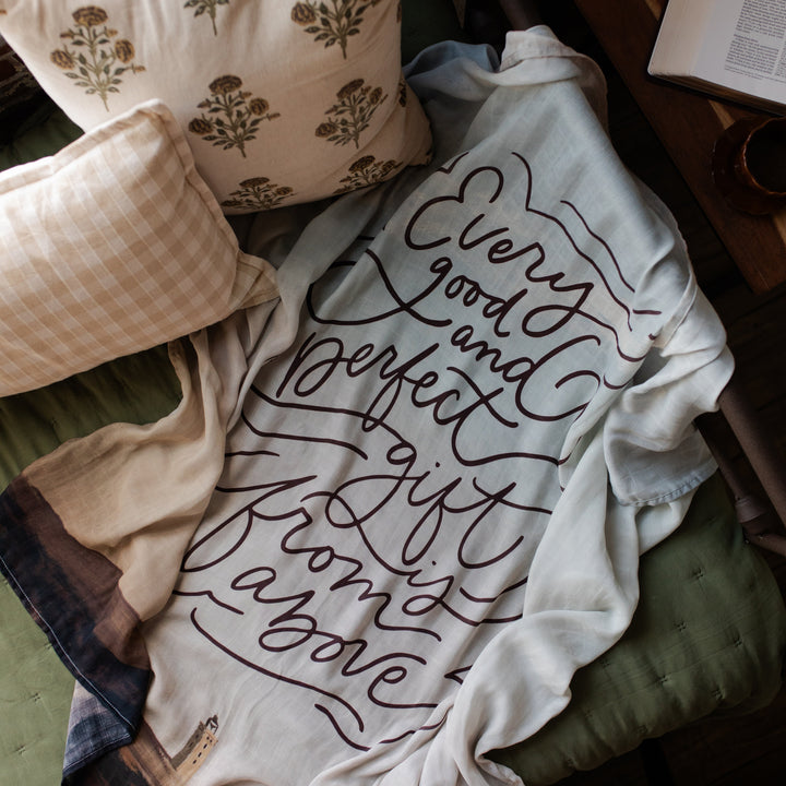 Good and Perfect Gift Swaddle on a green cushion next to two pillows