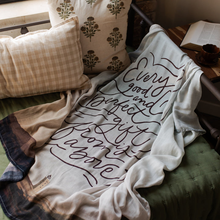Good and Perfect swaddle on a green cushion next to two pillows and an open bible