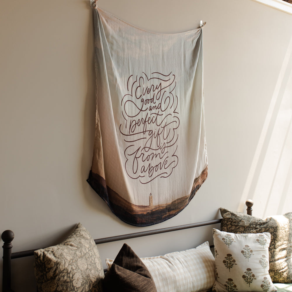 The Good and Perfect Gift Swaddle hanging over a couch with pillows