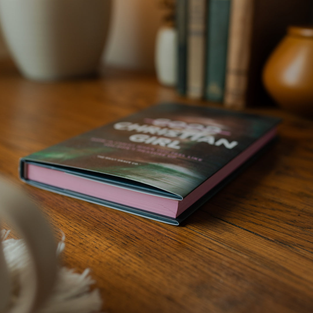 The Good Christian Girl Book cover on a wooden table near some vases
