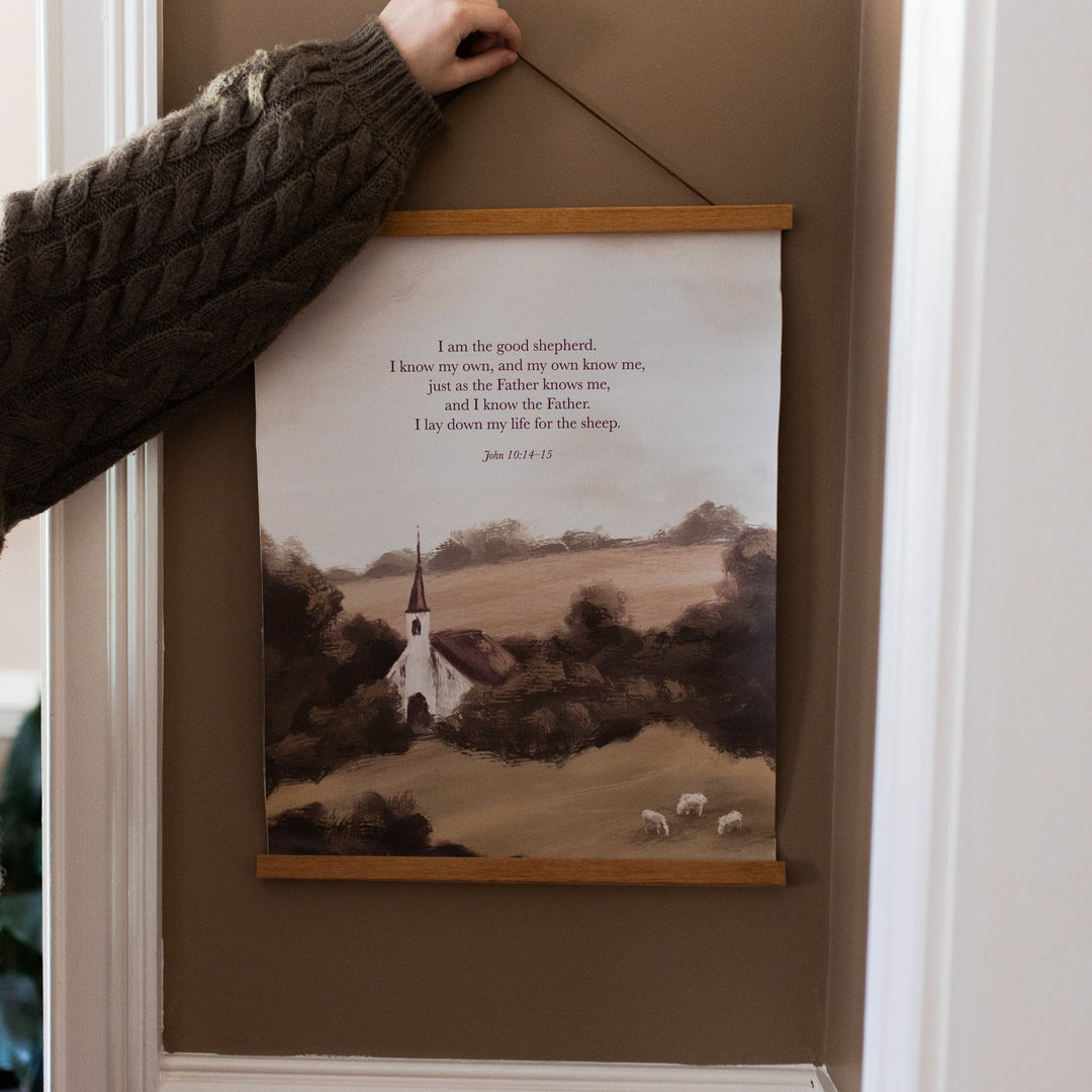 A woman holding up the Good Shepherd canvas print on a painted wall