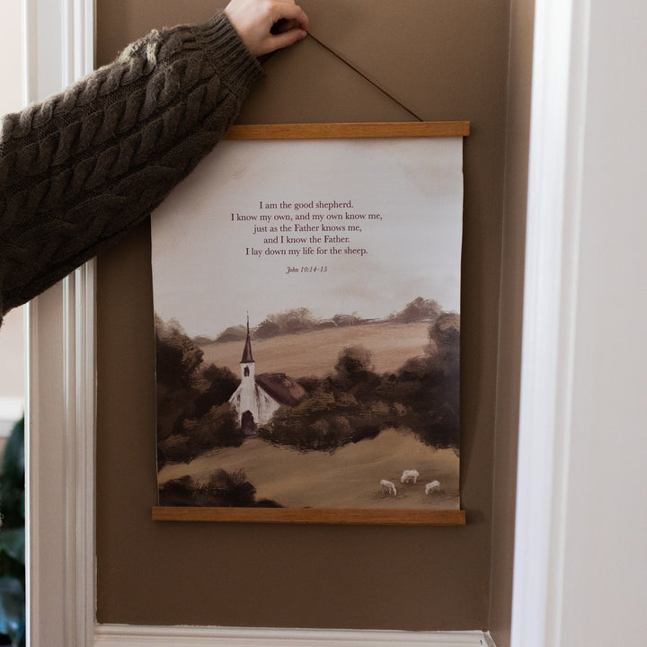 A woman holding up the Good Shepherd canvas print on a painted wall