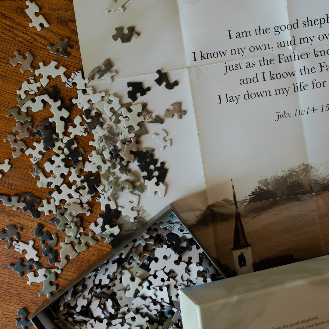 Good Shepherd Puzzle pieces next to the puzzle poster on a wooden table