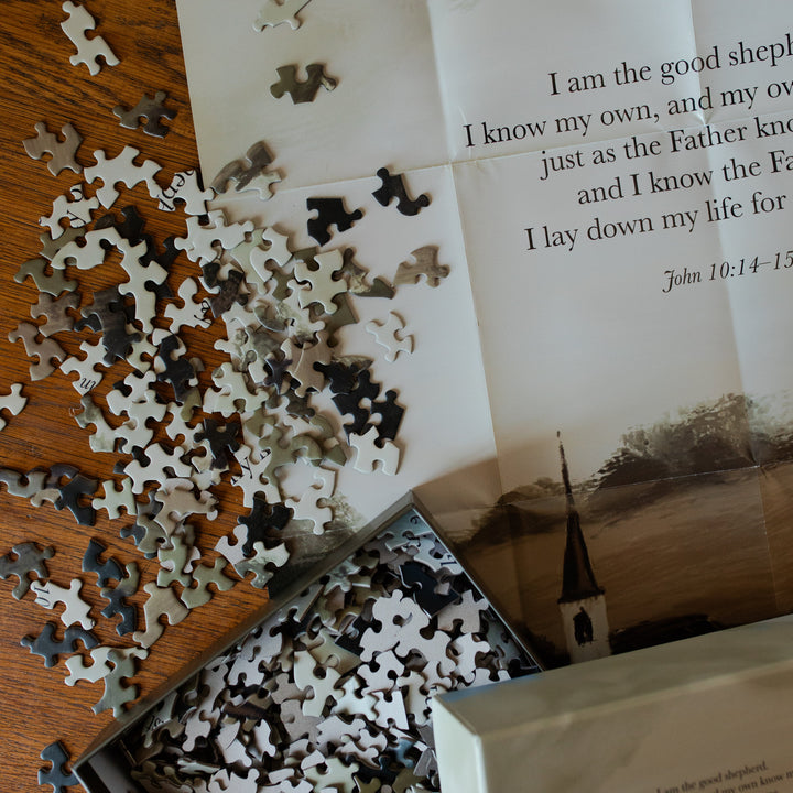 Good Shepherd Puzzle pieces next to the puzzle poster on a wooden table