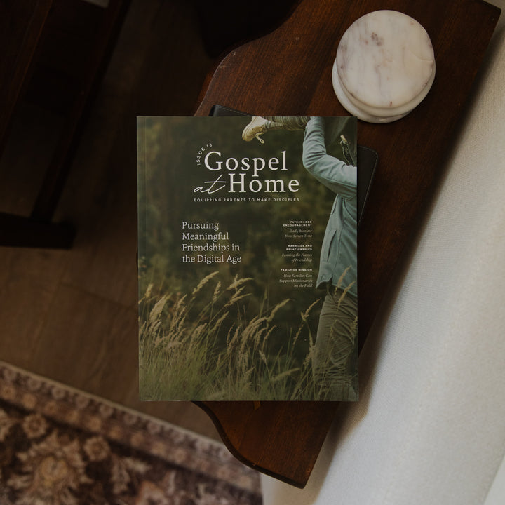 A magazine titled 'Gospel at Home' lies on a dark wooden table, partially covered by a black folder. The cover shows a person in a grassy field with the headline 'Pursuing Meaningful Friendships in the Digital Age.