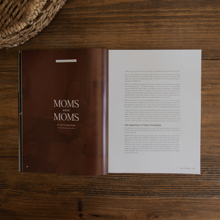 An open magazine page titled "Moms Who Moms" by Erica Richardson, featuring a dark brown cover on the left page and white text pages on the right, photographed flat on a dark wood tabletop with a woven basket edge visible in the top-left corner.