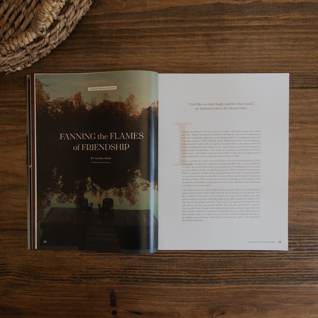An open magazine spread laid flat on a dark wood surface, showing a left page with a moody lake scene and the title 'FANNING the FLAMES of FRIENDSHIP' and a right page with a quote and body text.