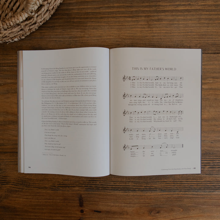 An open magazine laid flat on a wooden table, showing printed text on the left page and sheet music titled 'THIS IS MY FATHER'S WORLD' on the right page. A woven basket edge is visible in the top-left corner.