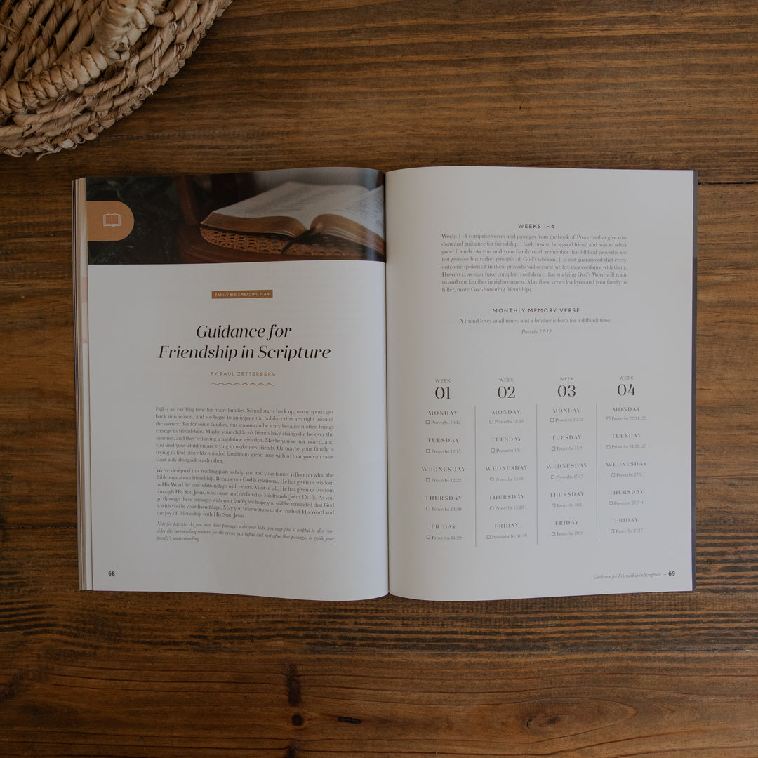 An open magazine laid flat on a wooden table, showing printed pages with text and a small photo of an open book. A woven basket edge is visible in the top left corner.