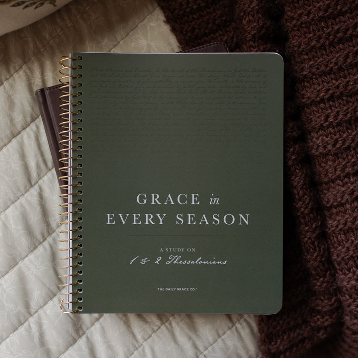 Notebook titled 'Grace in Every Season' on a textured surface with a knit blanket.