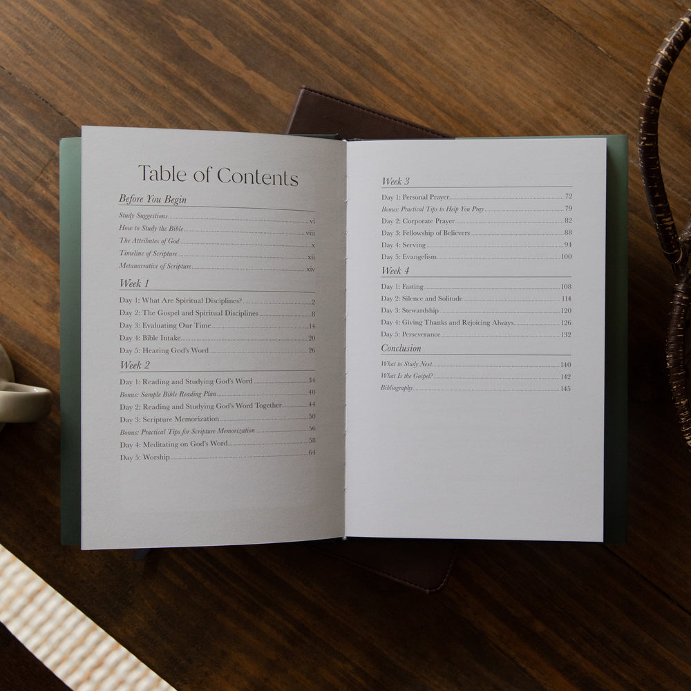 An open book showing the Table of Contents on both pages, photographed from above on a dark wooden table with a small brown leather item behind it.
