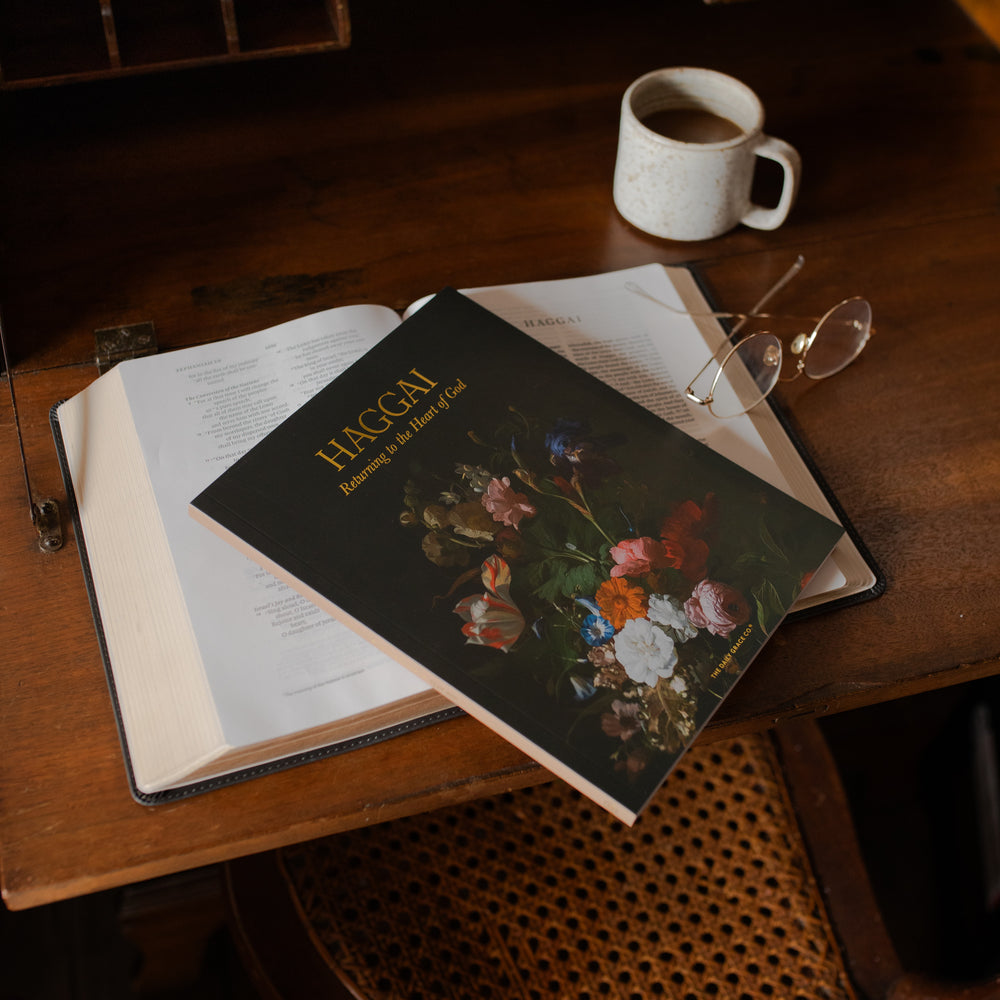 Haggai study cover on an open bible and a pair of eyeglasses on a wooden desk near a coffee cup