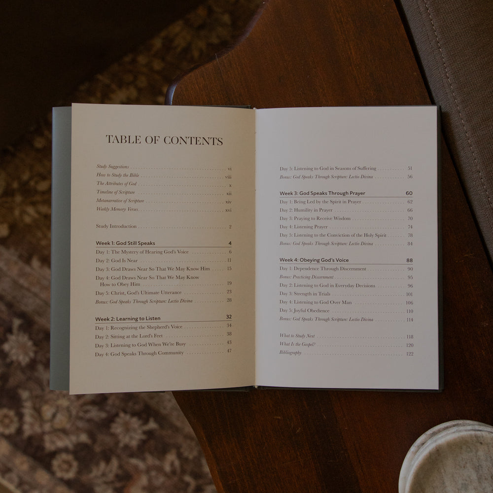 An open book showing a printed table of contents on both pages, placed on a dark wooden surface with a leather bag in the background.