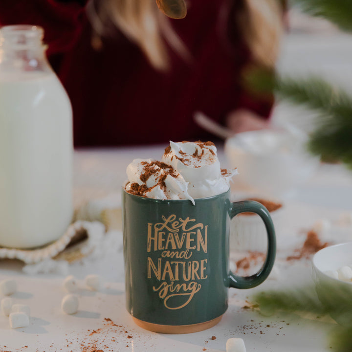 Woman pouring cinnamon on top of Heaven and Nature Sing Christmas mug in green