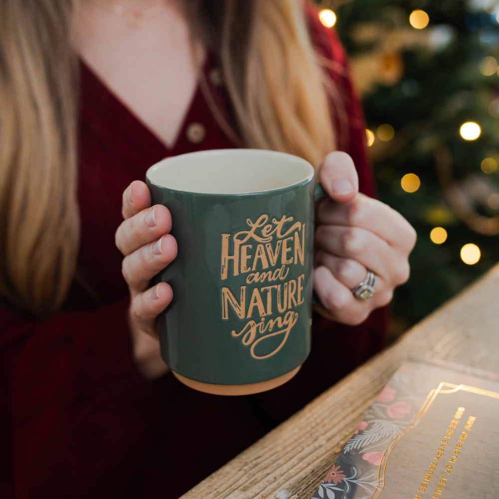 Woman holding Christmas mug that says Heaven and Nature Sing