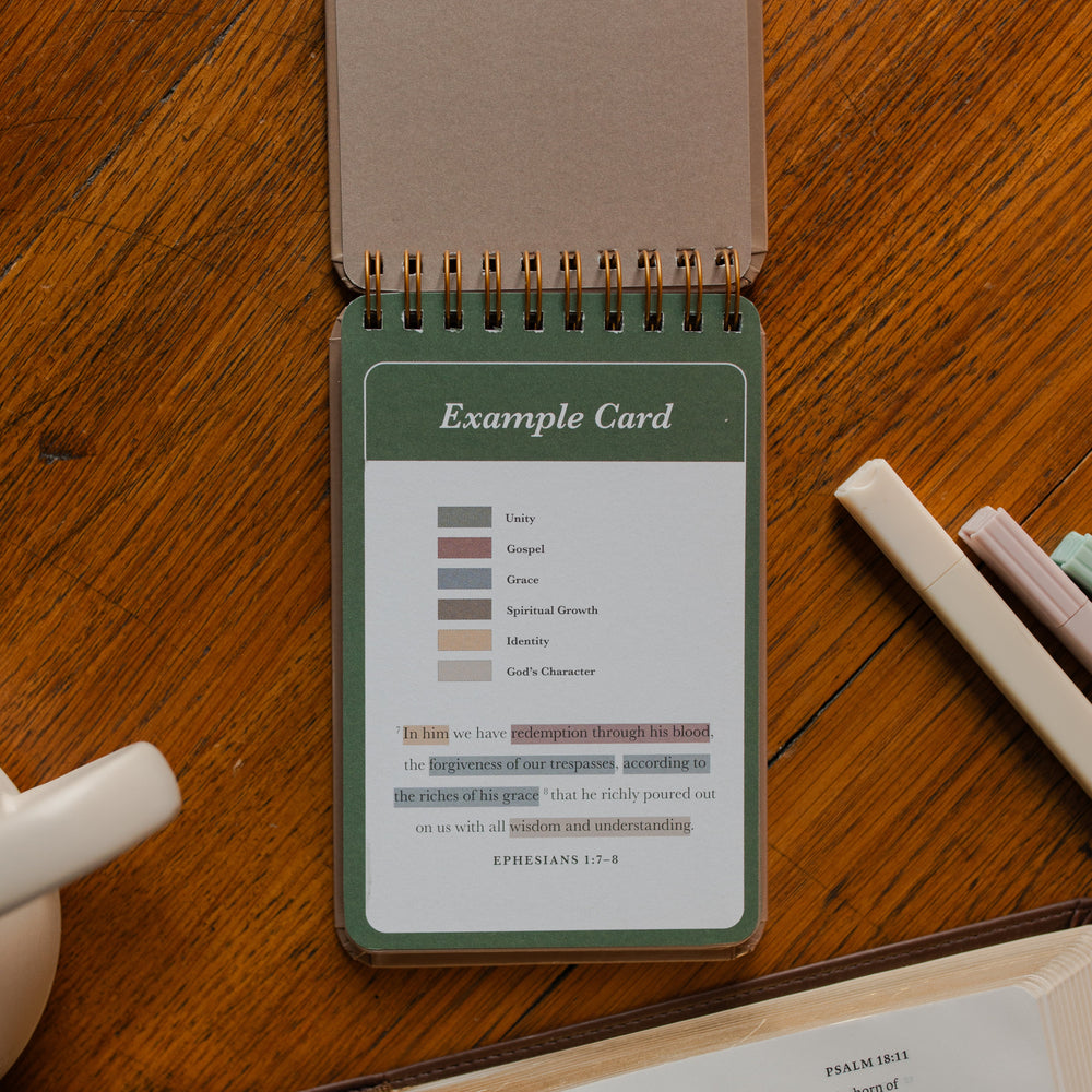 Highlighting through Scripture flipbook flipped to the Example Card near an open bible on a wooden table near some highlighters