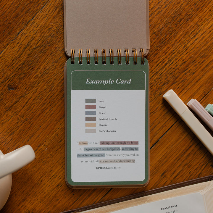 Highlighting through Scripture flipbook flipped to the Example Card near an open bible on a wooden table near some highlighters