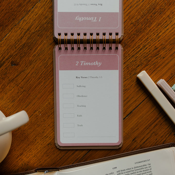 Highlighting through Scripture flipbook flipped to the 2 Timothy Card near an open bible on a wooden table near some highlighters