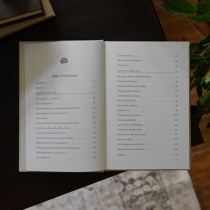His Love Endures Forever book opened to the table of contents page on a dark wooden table with some greenery nearby