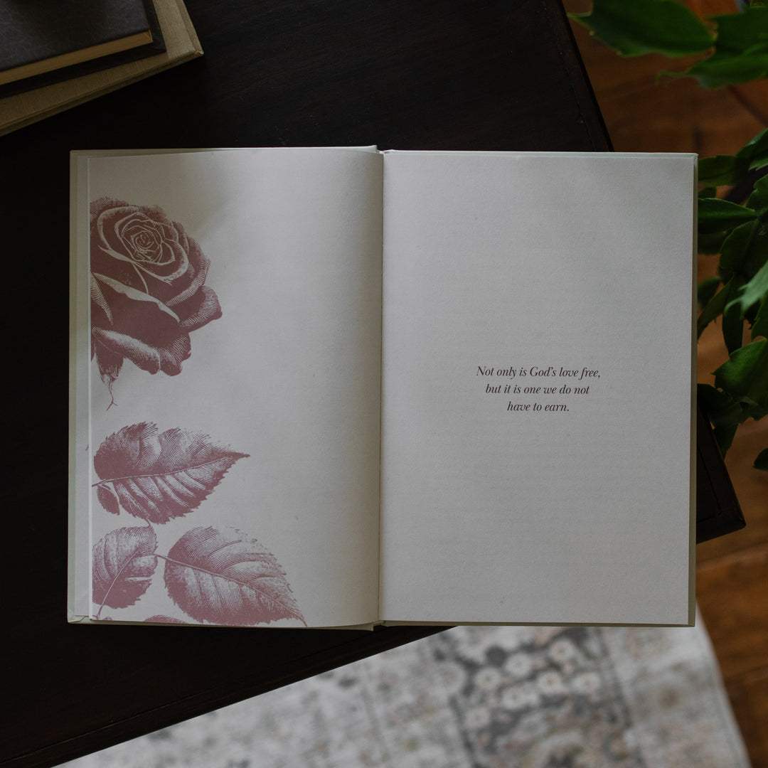 His Love Endures Forever book opened to the Not only is God's love free page on a dark wooden table with some greenery nearby