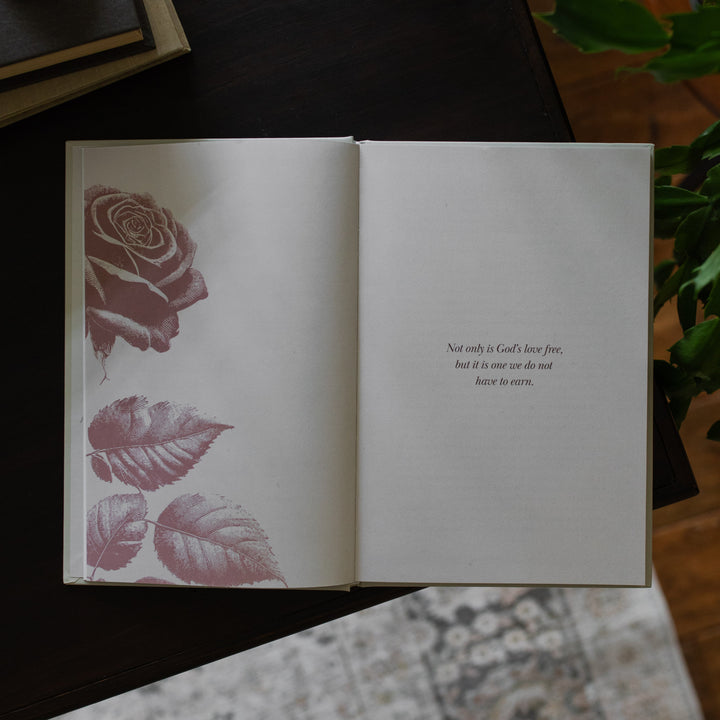 His Love Endures Forever book opened to the Not only is God's love free page on a dark wooden table with some greenery nearby