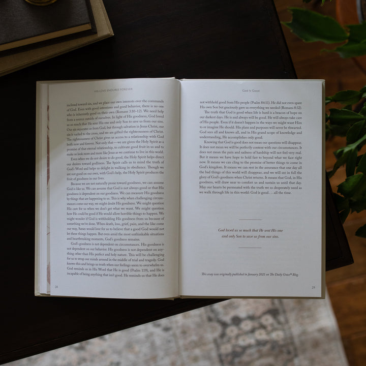His Love Endures Forever book opened to the God is Good ending paragraph page on a dark wooden table with some greenery nearby