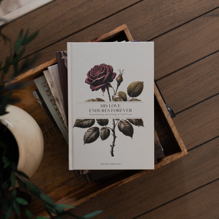 His Love Endures Forever book cover on a brown wooden table with some greenery nearby